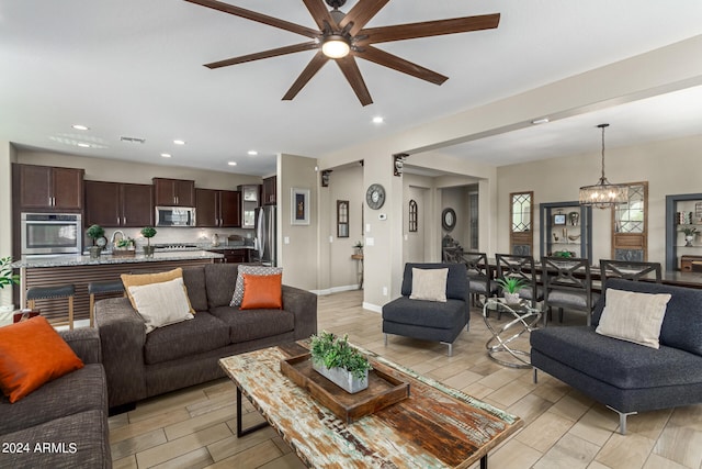 living room with light wood-type flooring, ceiling fan with notable chandelier, and sink