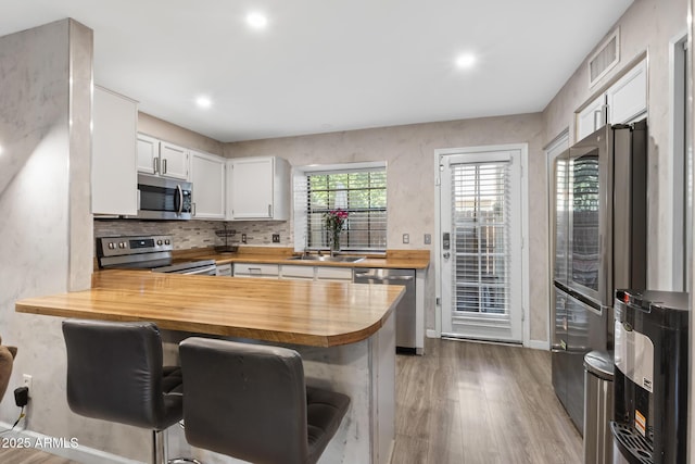 4901 E Kelton Ln Unit 1052, Scottsdale, AZ 85254 - kitchen with appliances with stainless steel finishes, butcher block counters, a peninsula, wood finished floors, and a breakfast bar area