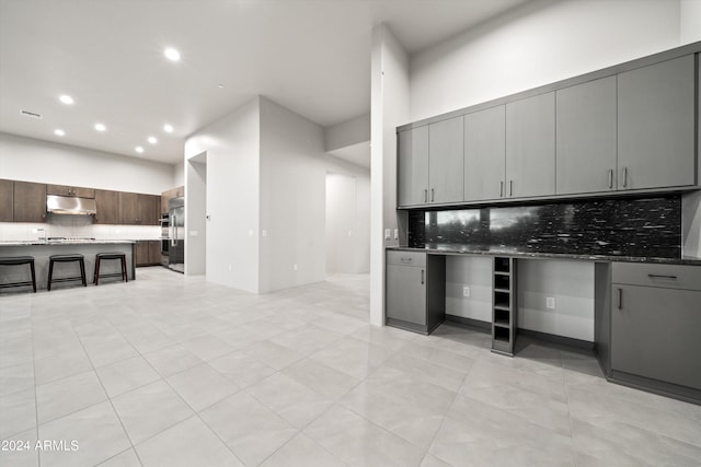 kitchen with backsplash, light tile patterned floors, dark stone countertops, gray cabinetry, and stainless steel built in fridge