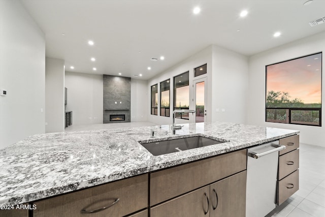 kitchen featuring a large fireplace, light stone counters, sink, light tile patterned flooring, and stainless steel dishwasher