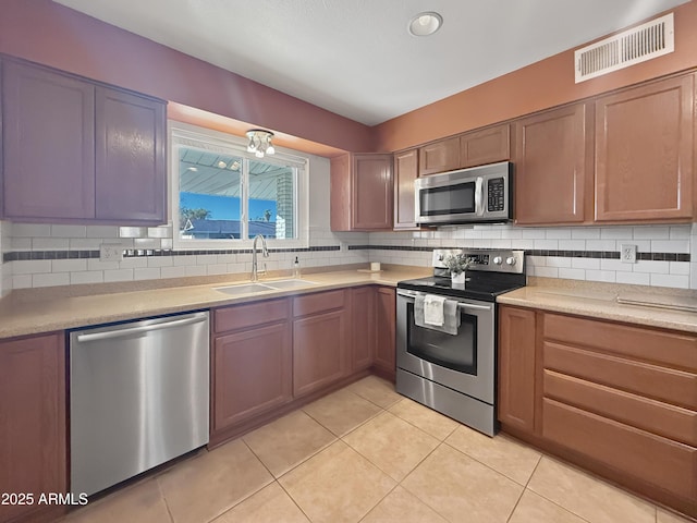 kitchen featuring appliances with stainless steel finishes, light tile patterned flooring, decorative backsplash, and sink