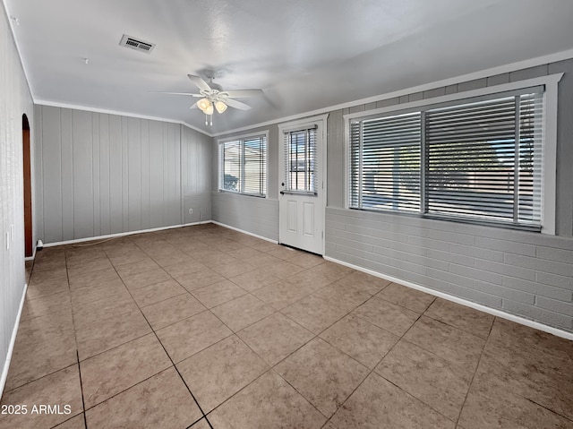 tiled spare room featuring brick wall, ceiling fan, and ornamental molding