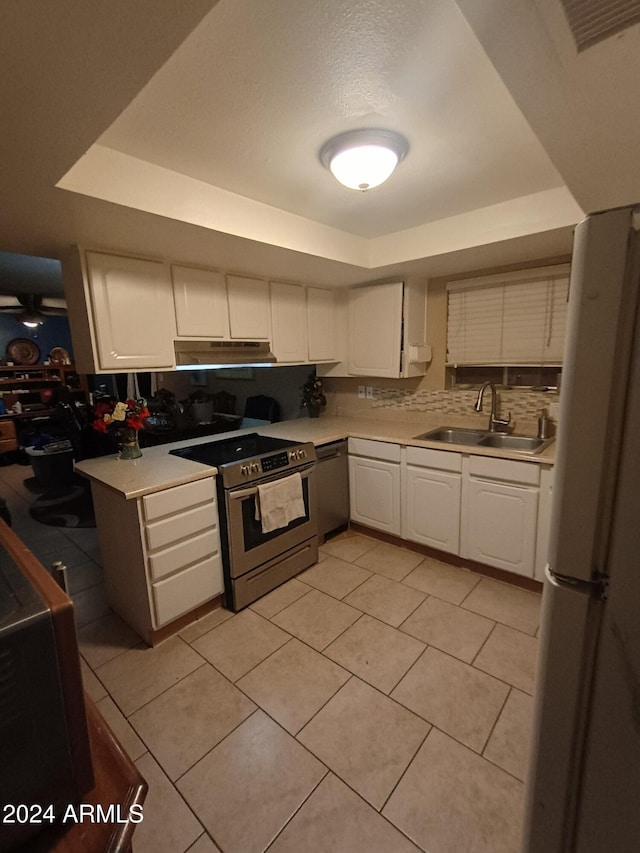 kitchen with a raised ceiling, sink, decorative backsplash, appliances with stainless steel finishes, and white cabinetry