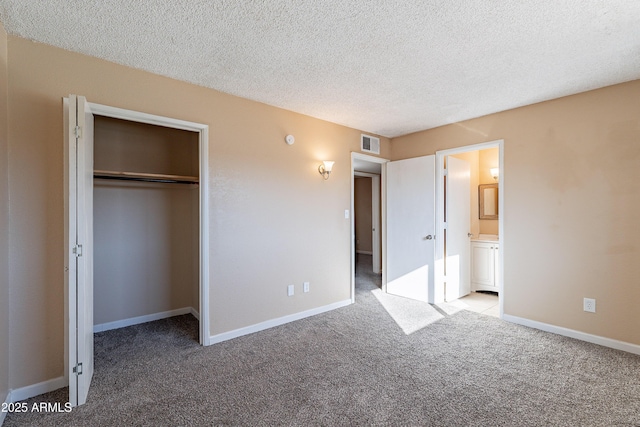 unfurnished bedroom with a textured ceiling, connected bathroom, light colored carpet, and a closet