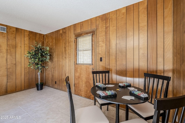 tiled dining room featuring a textured ceiling and wood walls