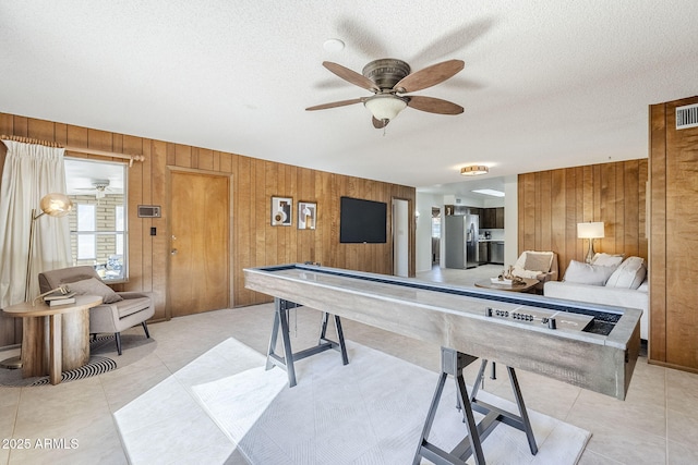 game room with wooden walls, a textured ceiling, and light tile patterned floors