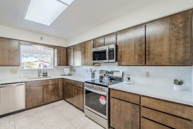 kitchen with a skylight, sink, backsplash, light tile patterned floors, and stainless steel appliances