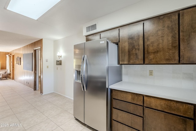 kitchen featuring backsplash, wooden walls, a skylight, stainless steel refrigerator with ice dispenser, and light tile patterned flooring