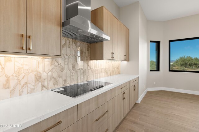 kitchen with light brown cabinets, black electric cooktop, wall chimney exhaust hood, light hardwood / wood-style floors, and tasteful backsplash