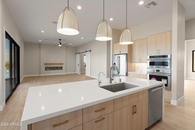 kitchen with sink, a barn door, hanging light fixtures, stainless steel appliances, and a kitchen island with sink