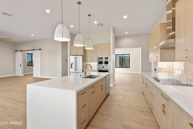 kitchen featuring an island with sink, hanging light fixtures, stainless steel appliances, sink, and a barn door