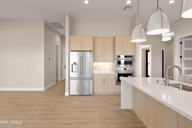 kitchen with hanging light fixtures, appliances with stainless steel finishes, light brown cabinetry, light wood-type flooring, and sink