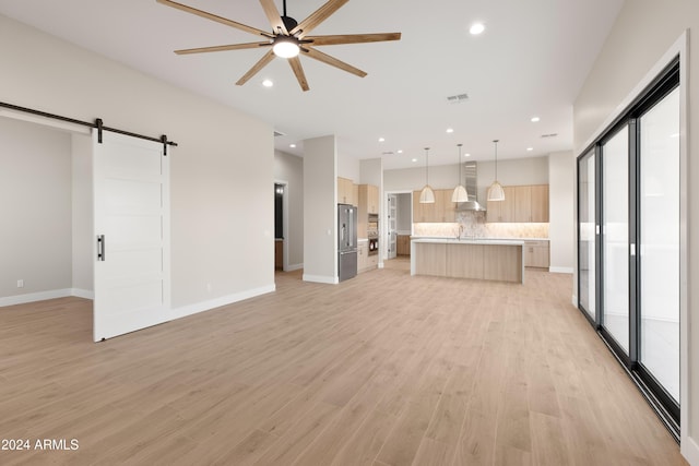 unfurnished living room featuring a barn door, light hardwood / wood-style floors, and ceiling fan