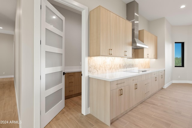 kitchen featuring light brown cabinets, black electric cooktop, wall chimney exhaust hood, light wood-type flooring, and tasteful backsplash