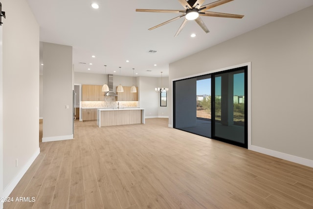 unfurnished living room with ceiling fan with notable chandelier, light hardwood / wood-style floors, sink, and a barn door