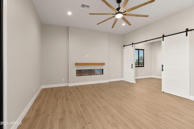 unfurnished living room featuring light hardwood / wood-style flooring, a barn door, and ceiling fan