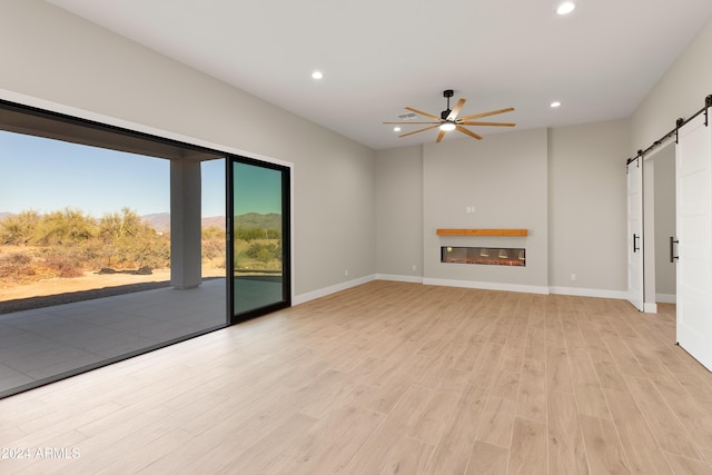 unfurnished living room featuring a barn door, light wood-type flooring, and ceiling fan