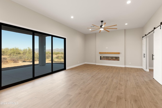 unfurnished living room with a barn door, light wood-type flooring, and ceiling fan