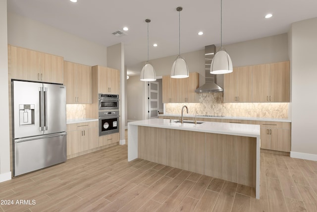 kitchen featuring appliances with stainless steel finishes, sink, light wood-type flooring, wall chimney exhaust hood, and decorative light fixtures