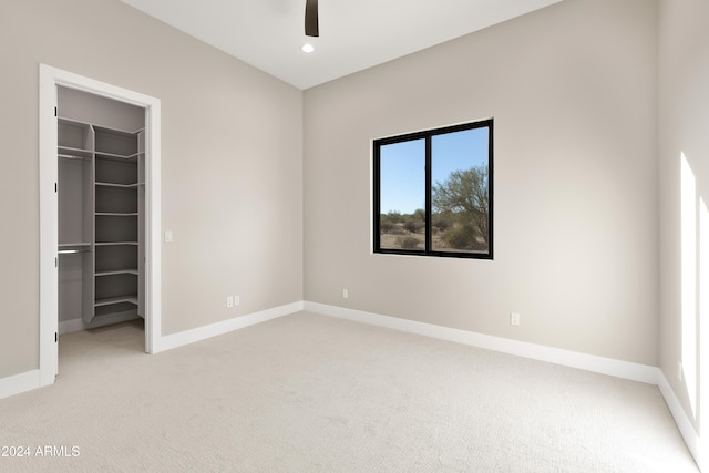 unfurnished bedroom featuring light carpet, a closet, a spacious closet, and ceiling fan