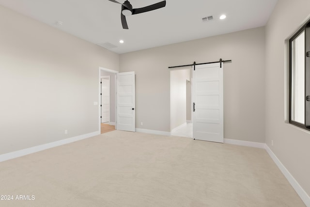 unfurnished bedroom featuring light carpet, a barn door, and ceiling fan