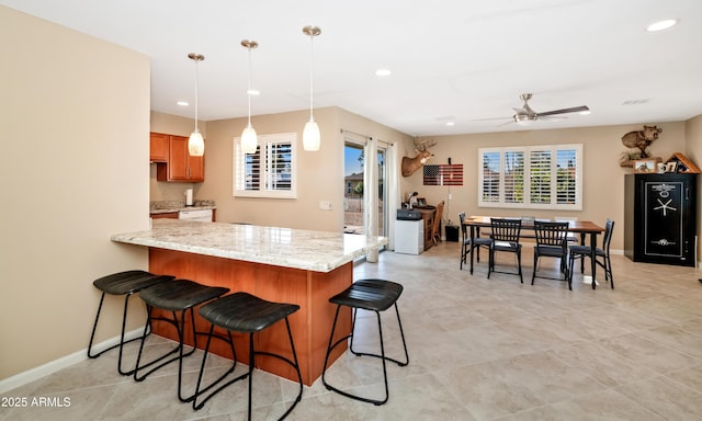 kitchen featuring baseboards, a breakfast bar, a peninsula, light stone countertops, and pendant lighting