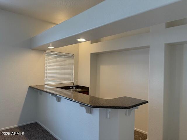 bar featuring a sink, dark colored carpet, and baseboards