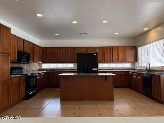kitchen with black appliances, visible vents, dark countertops, and a kitchen island