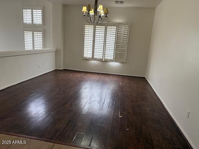 empty room featuring wood finished floors, a chandelier, visible vents, and baseboards