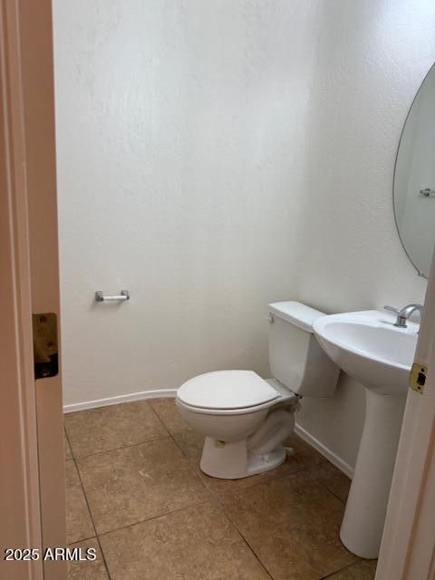 half bathroom featuring tile patterned floors, toilet, and baseboards