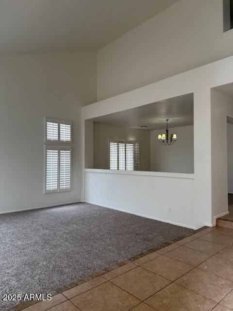 carpeted empty room with a towering ceiling, tile patterned flooring, a notable chandelier, and baseboards