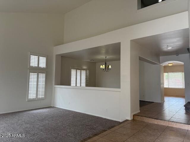 empty room with an inviting chandelier, tile patterned floors, carpet, baseboards, and arched walkways