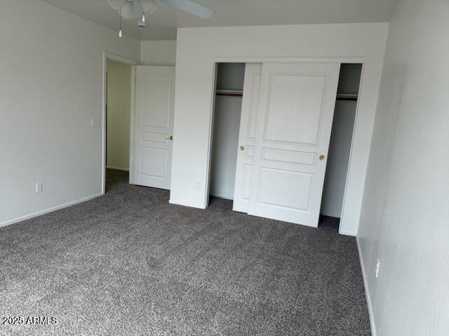 unfurnished bedroom with baseboards, dark carpet, ceiling fan, and a closet