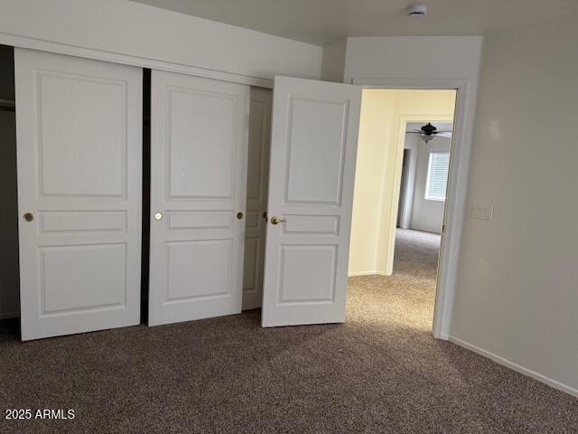 unfurnished bedroom with dark colored carpet, baseboards, and a closet