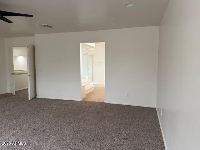 spare room with light colored carpet, visible vents, a ceiling fan, and baseboards