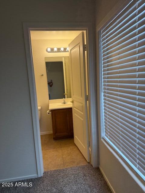 hall with light tile patterned flooring, a sink, light carpet, and baseboards