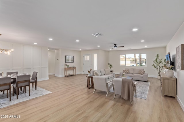 living room featuring recessed lighting, ceiling fan with notable chandelier, visible vents, baseboards, and light wood-type flooring