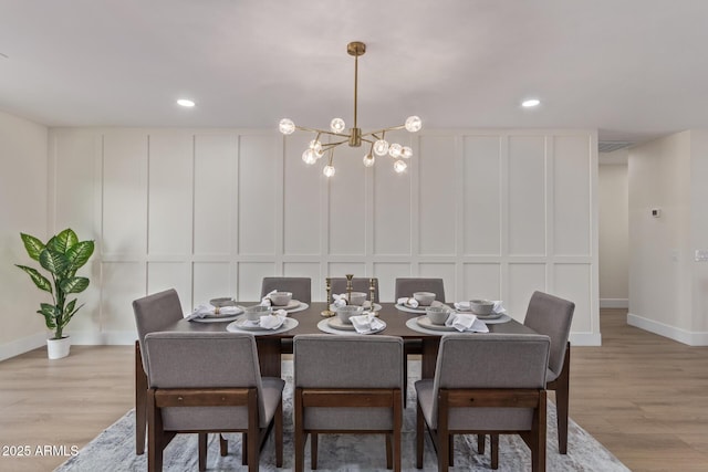 dining space featuring recessed lighting, a decorative wall, light wood finished floors, and an inviting chandelier