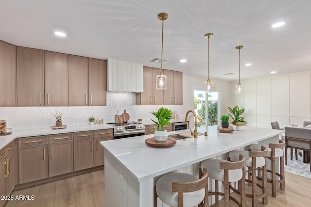 kitchen featuring light wood finished floors, decorative backsplash, a breakfast bar area, stainless steel electric range, and a sink