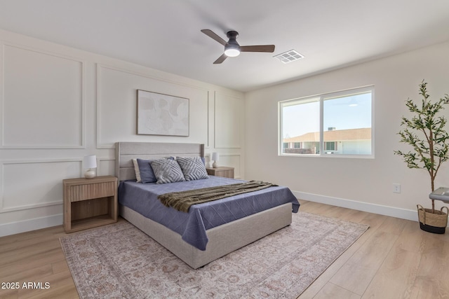 bedroom with baseboards, light wood finished floors, visible vents, and a decorative wall