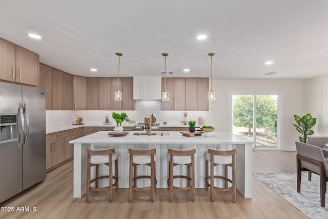 kitchen featuring a breakfast bar area, light countertops, backsplash, light wood-style floors, and stainless steel fridge