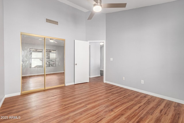 unfurnished bedroom featuring hardwood / wood-style flooring, ceiling fan, a high ceiling, and a closet