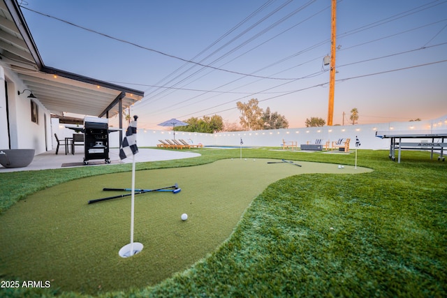 yard at dusk with a putting area, a patio, and fence