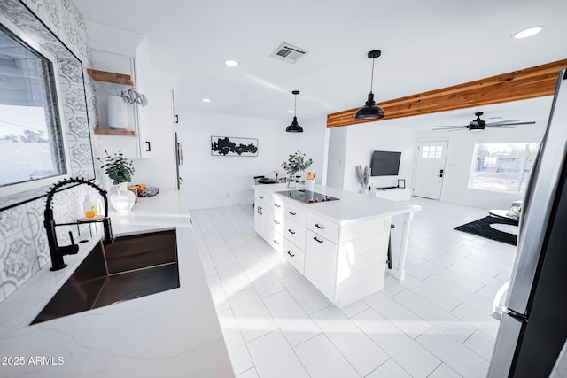 kitchen with a sink, black electric stovetop, white cabinets, freestanding refrigerator, and hanging light fixtures