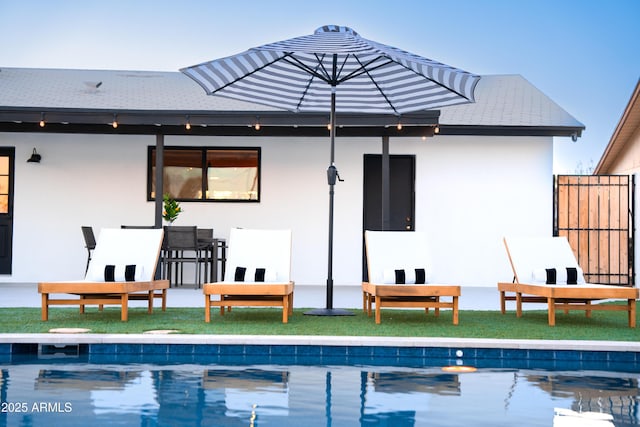 rear view of property with stucco siding, an outdoor pool, and fence