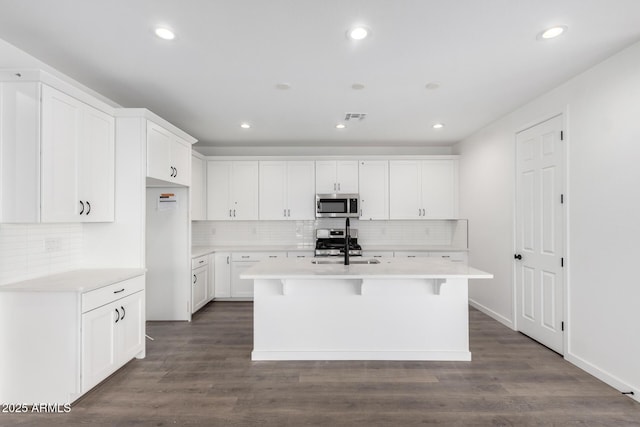 kitchen with white cabinetry, dark wood-type flooring, stainless steel appliances, a breakfast bar area, and a center island with sink