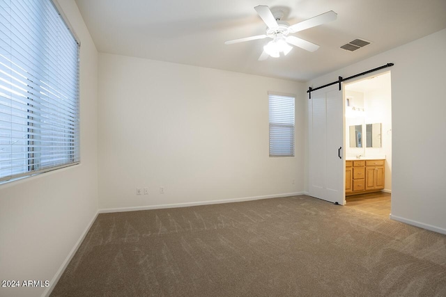 unfurnished bedroom featuring a barn door, ceiling fan, ensuite bath, and multiple windows