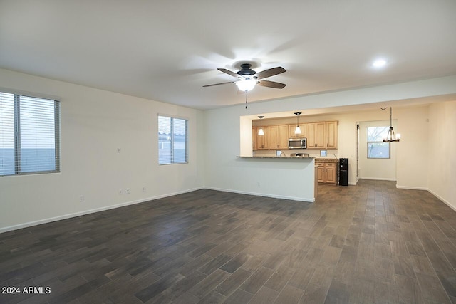 unfurnished living room with ceiling fan with notable chandelier, dark hardwood / wood-style flooring, and a wealth of natural light