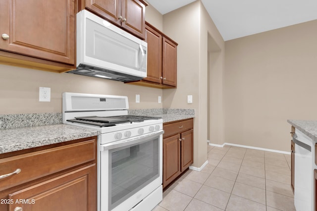 kitchen featuring brown cabinets, white appliances, light tile patterned flooring, and baseboards