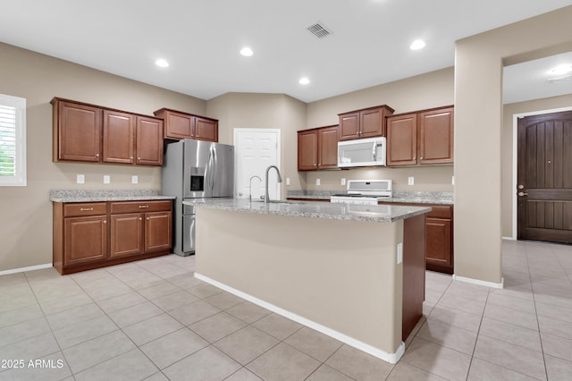 kitchen with white appliances, an island with sink, light stone countertops, a sink, and light tile patterned flooring